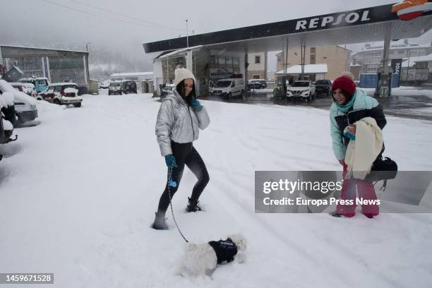 Two women walk with their dog along a snow-covered street on January 26 in Pedrafita do Cebreiro, Lugo, Galicia, Spain. There is a corridor formed by...