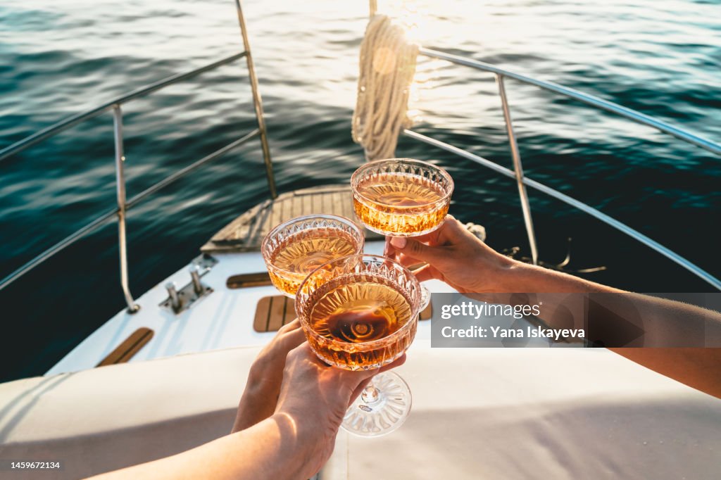 A close-up shot of friends clinking sparkling wine glasses at sunset on a yacht