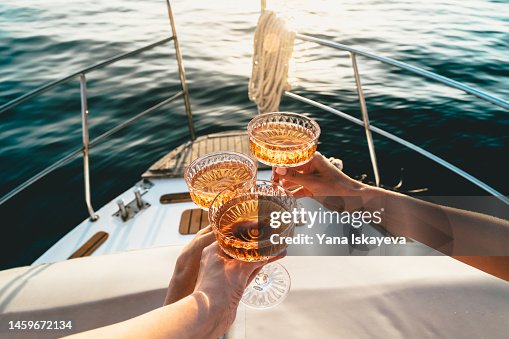 A close-up shot of friends clinking sparkling wine glasses at sunset on a yacht A close-up shot of friends clinking sparkling wine glasses at sunset on a yacht