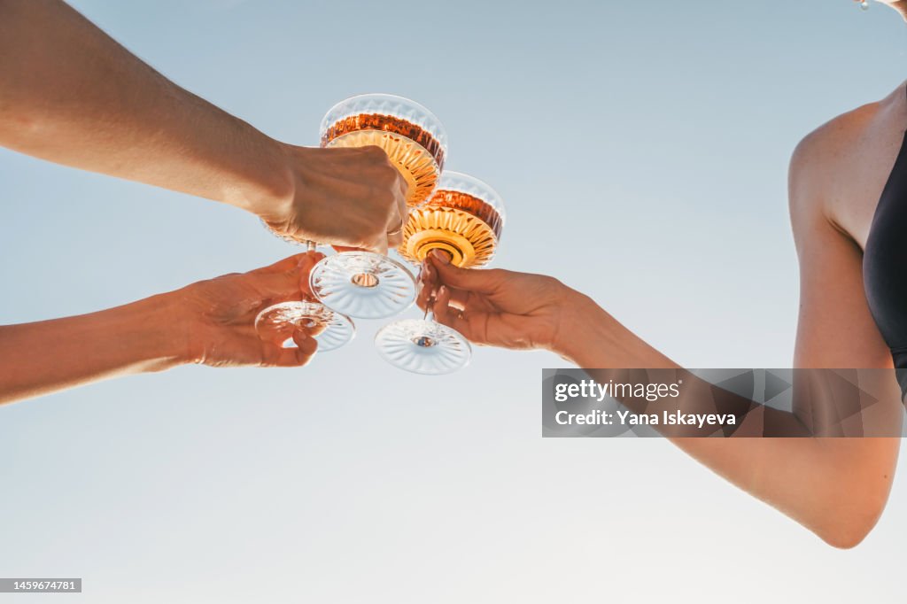 A close-up shot of friends clinking sparkling wine glasses at sunset