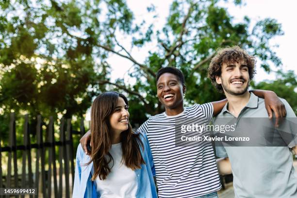 united multiracial friends having fun embracing and walking together outdoor - three people walking stock pictures, royalty-free photos & images