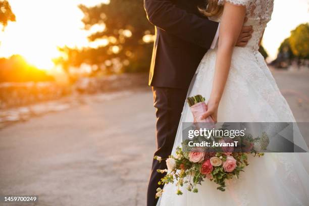 bride and groom hugging with wedding  bouquet in her hand - white wedding dress stock pictures, royalty-free photos & images