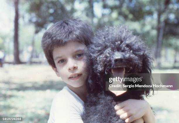 vintage photo of a young boy and his black dog in a park in caracas, venezuela, 1983 - boys photos stock-fotos und bilder