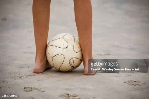 legs of a young adult woman holding an old soccer ball on the beach sand - sand trap stockfoto's en -beelden