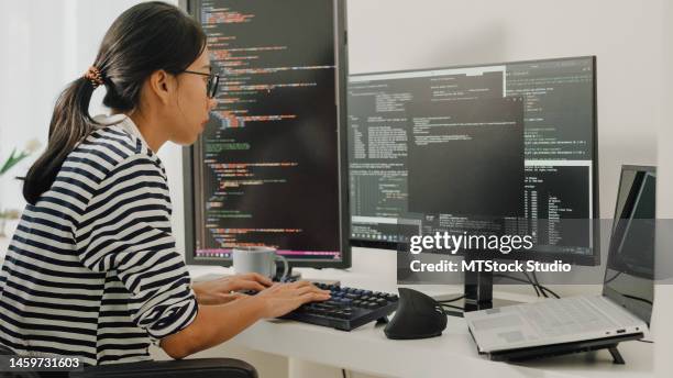 young asian woman software developers using computer to write code sitting at desk with multiple screens work remotely at home. - data scientist stock pictures, royalty-free photos & images