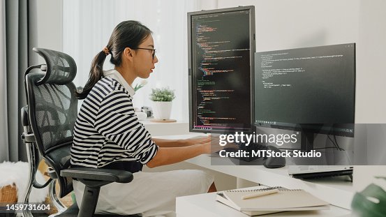 Young Asian woman software developers using computer to write code sitting at desk with multiple screens work remotely at home. Young Asian woman software developers using computer to write code sitting at desk with multiple screens work remotely at home.