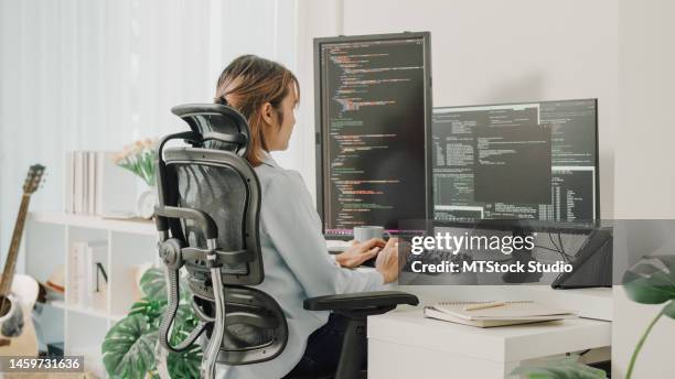 young asian woman software developers using computer to write code sitting at desk with multiple screens work remotely at home. - datawetenschapper stockfoto's en -beelden
