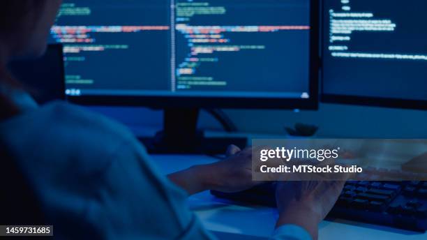 closeup of young asian woman software developers using computer to write code sitting at desk with multiple screens work remotely in home at night. - application programming interface stockfoto's en -beelden