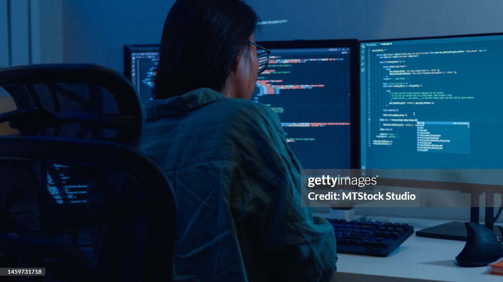 Giovani sviluppatrici di software asiatiche che utilizzano il computer per scrivere codice sedute alla scrivania con più schermi lavorano in remoto a casa di notte.