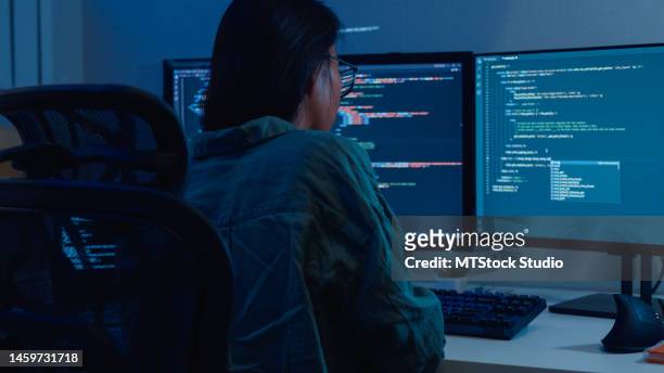 young asian woman software developers using computer to write code sitting at desk with multiple screens work remotely in home at night. - development and coding stockfoto's en -beelden