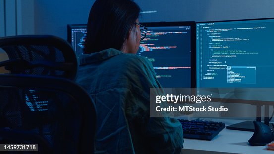 Young Asian woman software developers using computer to write code sitting at desk with multiple screens work remotely in home at night. Young Asian woman software developers using computer to write code sitting at desk with multiple screens work remotely in home at night.