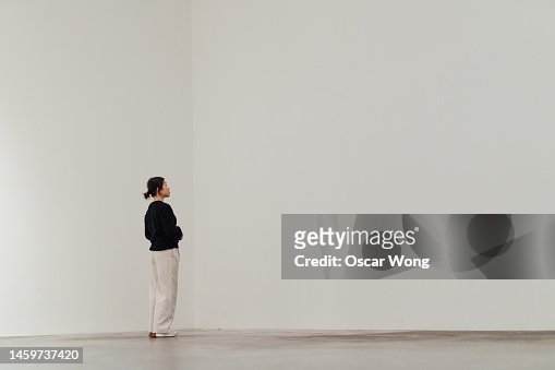 Full length of young Asian woman looking away while standing against white wall