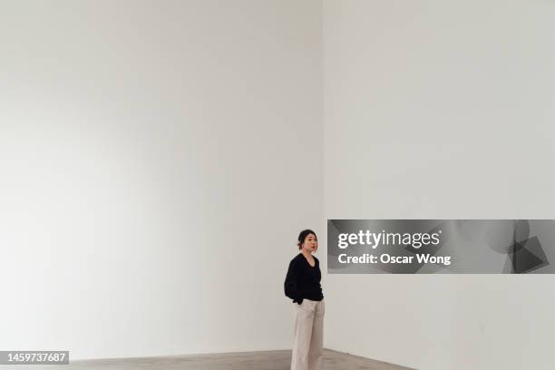 full length of young asian woman looking away while standing against white wall - stand exposition stock pictures, royalty-free photos & images