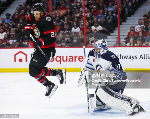 Mathieu Joseph of the Ottawa Senators jumps in the air as he attempts to screen Connor Hellebuyck of the Winnipeg Jets during the second period of...