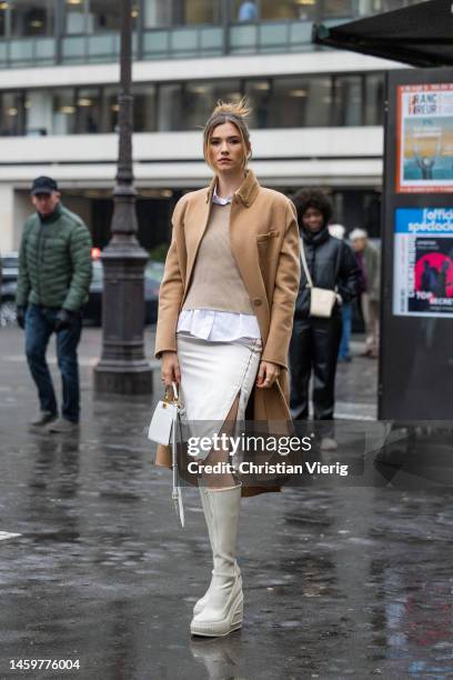 Zita d'Hauteville wears brown coat, white skirt with slit, creme white knee high boots, white bag, button shirt, jumper outside Fendi during Paris...