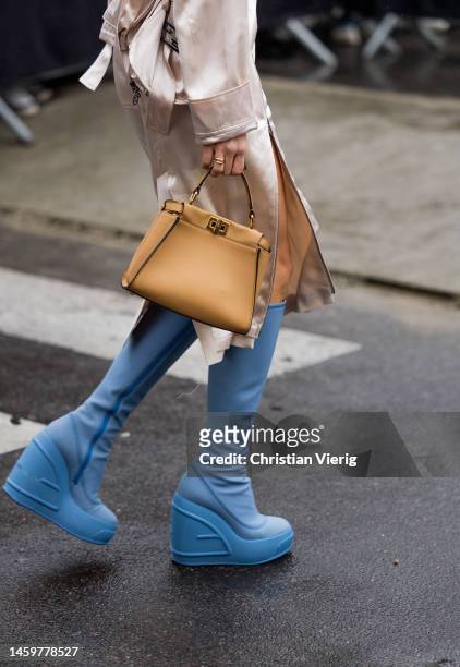 Caroline Caro Daur wears brown bag, creme white silk skirt with slit, jacket, white shirt, golden necklace, knee high blue boots outside Fendi during...