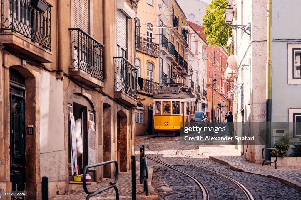 Historic yellow tram on a steep street in Alfama district, Lisbon, Portugal