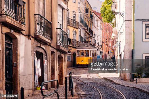 historic yellow tram on a steep street in alfama district, lisbon, portugal - tram foto e immagini stock