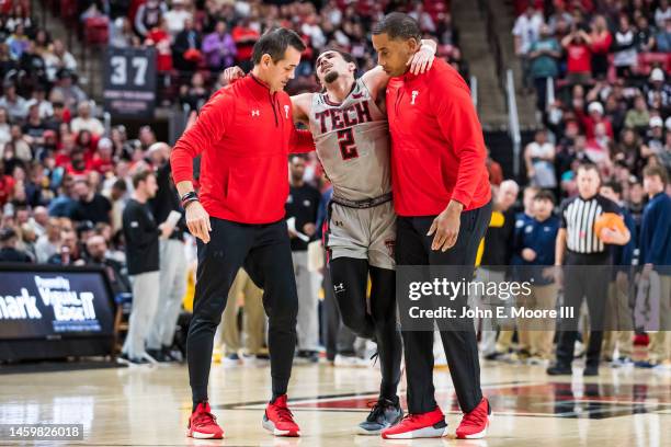 Guard Pop Isaacs of the Texas Tech Red Raiders is helped off the court by athletic trainer Mike Neal and strength and conditioning coach Darby Rich...
