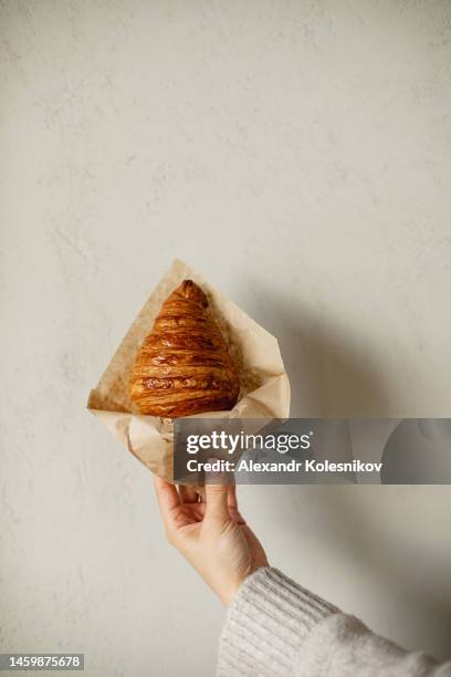 female hand holding fresh croissant in paper bag. concept of delivery food, small business. copy space - brioche foto e immagini stock