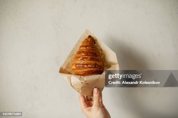 female hand holding fresh croissant in paper bag. concept of delivery food, small business. copy space - breaking croissant stock pictures, royalty-free photos & images