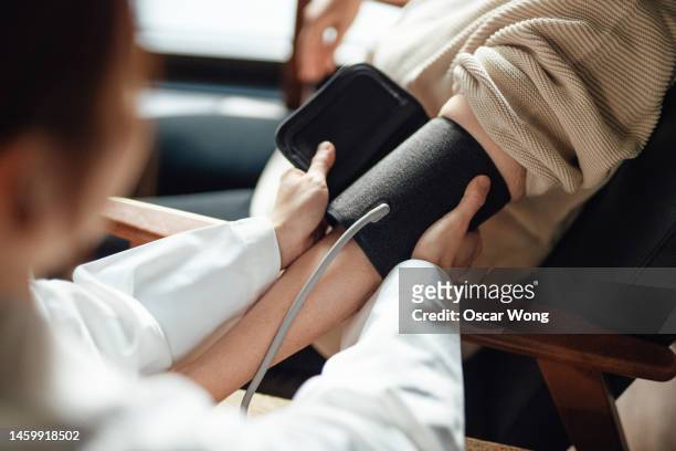 over the shoulder view of nurse checking blood pressure for patient - hypertension stock-fotos und bilder