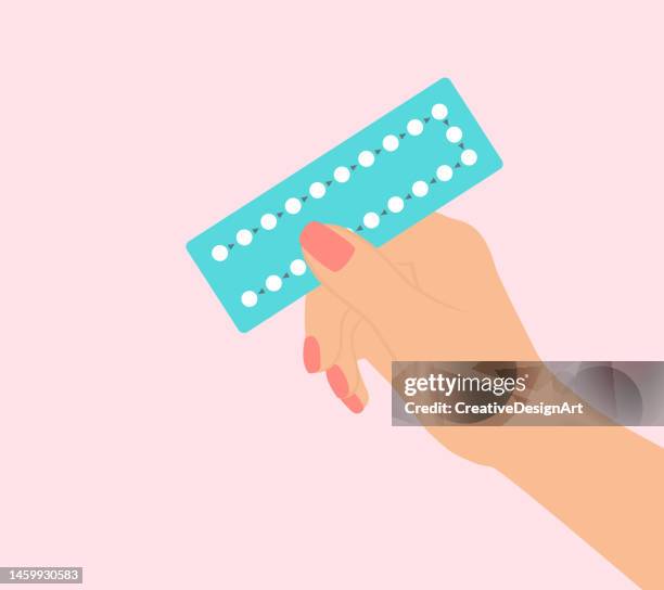 female hand holding birth control pills on pink background - contraceptive pills stock illustrations