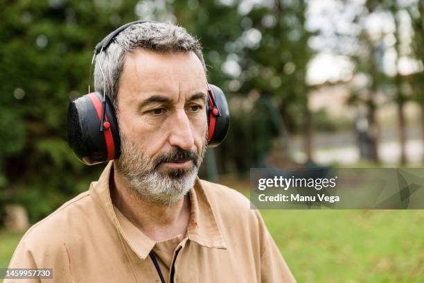 male using ear protection while working outdoors in a garden. - idrottsplatspersonal bildbanksfoton och bilder