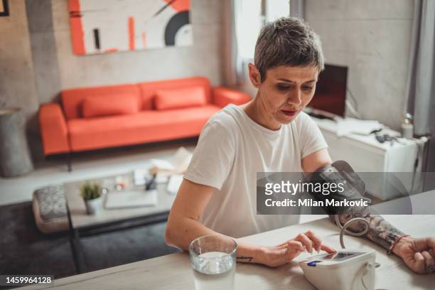 a mature woman measures blood pressure on a digital meter - altitude sickness stock pictures, royalty-free photos & images