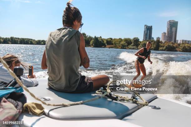 adult female coach sitting on stern during wake surf training - wasserski stock-fotos und bilder