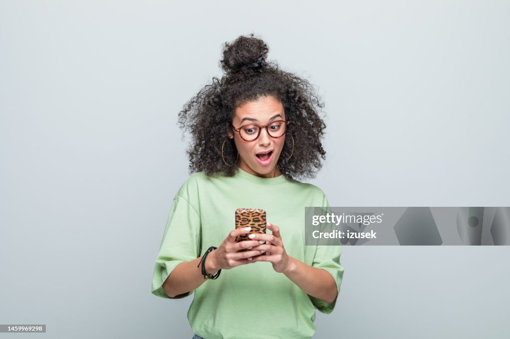 Portrait of surprised young woman using phone
