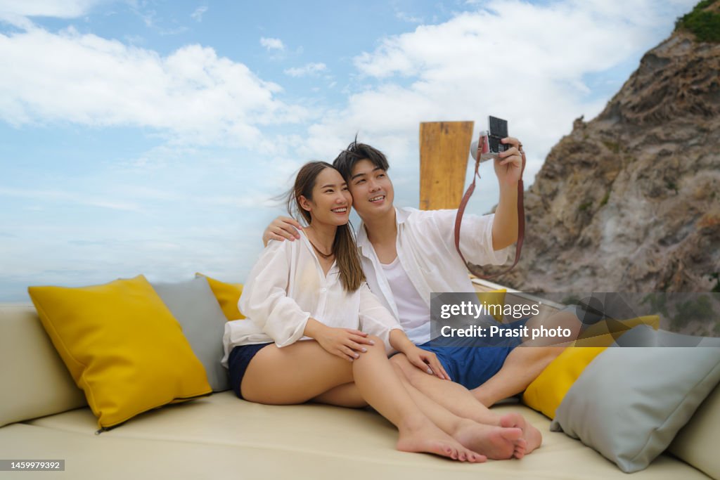 Asian couple taking a selfie on camera sitting on longtail boat during thier summer vacation in Phuket,Thailand