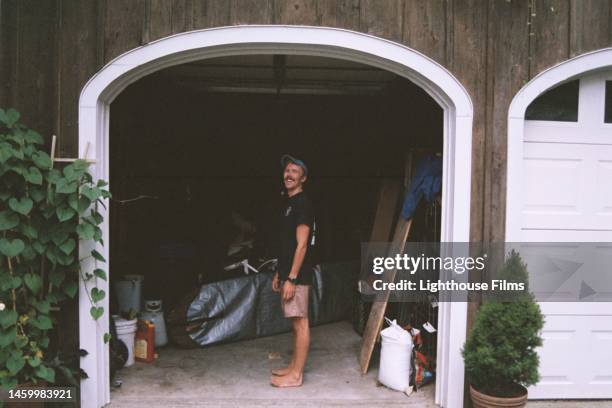 a young man stands within the frame of his garage. - old garage at home stock pictures, royalty-free photos & images