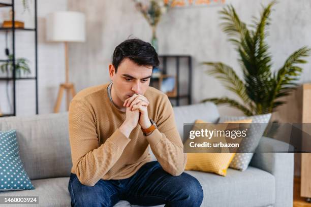 sad young man sitting on the sofa at home - frustration stock pictures, royalty-free photos & images