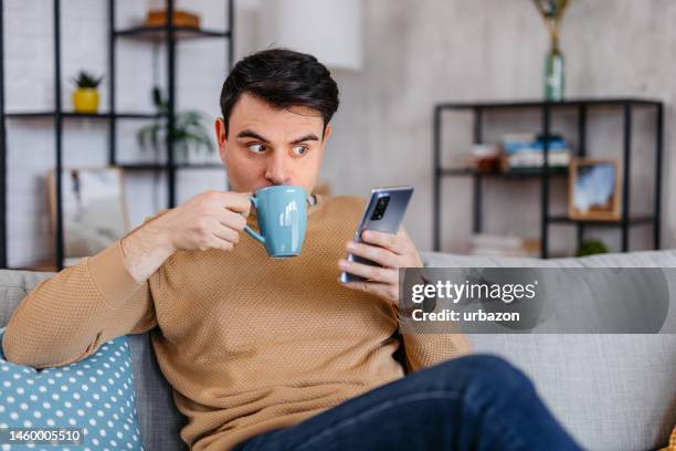 joven recibiendo un mensaje de texto sorprendente en casa - hombre asombrado fotografías e imágenes de stock