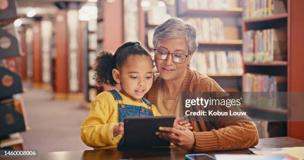 biblioteca infantil, familiar negra y tableta para el desarrollo del aprendizaje en línea con educación y lectura. mujer mayor enseñando a niña mientras transmite sitio web, libro electrónico y libros para aprender conocimientos juntos - lector de libros electrónicos fotografías e imágenes de stock