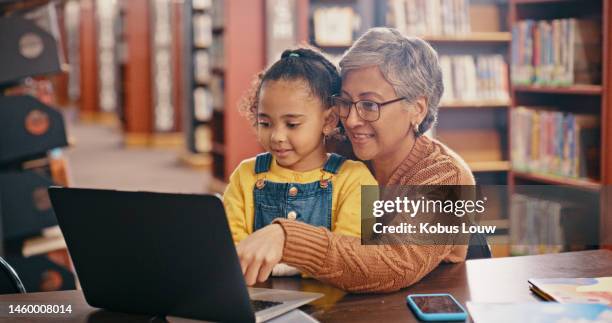 child, grandmother and laptop while reading ebook for online and distance learning together at library. senior woman teaching girl or family while streaming video for education, books and knowledge - old video library stockfoto's en -beelden