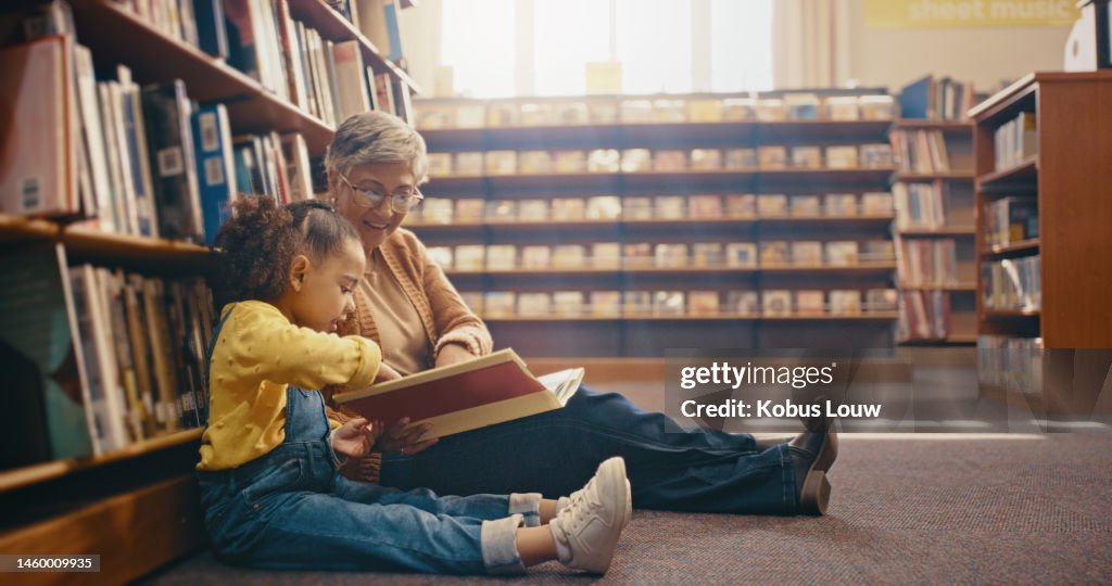 Library, learning and grandmother with grandchild on floor with book for reading, story and fun together. Education, child development and grandma with girl, storytelling and teaching while bonding