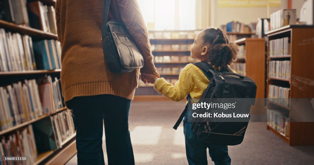Library, help child and woman search books, learning and education support and holding hands for fun hobby. Kindergarten girl and family or people by bookshelf for back to school and mind development