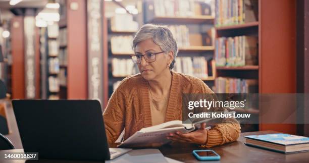 senior woman, computer and planning in a library with book and laptop for lecture class. teacher, university professor and education worker reading web data and research for class on a study desk - bibliotecário imagens e fotografias de stock