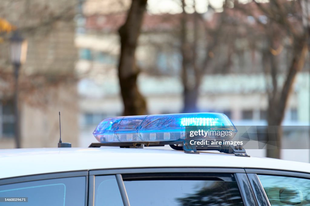 A close-up view of a police vehicle with blue lights patrolling near a public park with the windows and doors closed