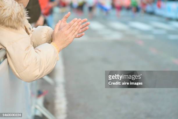young girl in jacket clapping her hands while watching the christmas parade in the city during the day. - parade watchers stock pictures, royalty-free photos & images