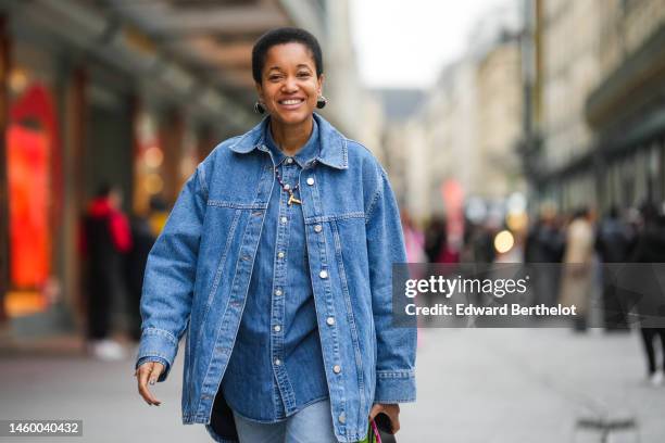 Tamu McPherson wears black and gold pendant earrings, a black / pink pearls and gold T pendant necklace, a blue denim buttoned shirt, a blue denim...