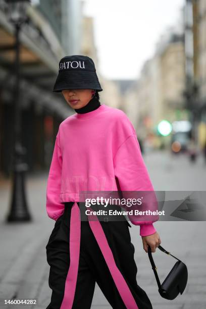 Alex Goya wears a black with white logo pattern bob from Patou, pink rose flower pattern earrings, a black turtleneck pullover, a neon pink sweater...