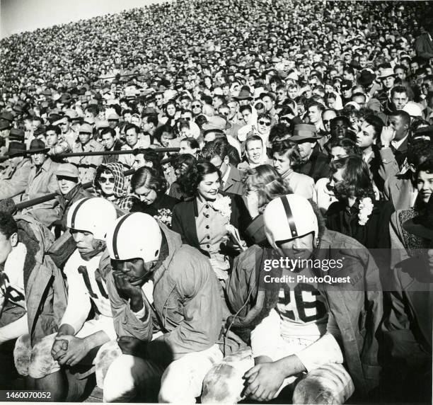 View of football players on the bench and the crowded grandstand at Michigan State College during a college football game , East Lansing, Michigan,...