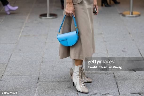 Suzi de Givenchy wears beige button up jacket, mid skirt, blue bag, laced boots outside Patou at La Samaritaine on January 27, 2023 in Paris, France.