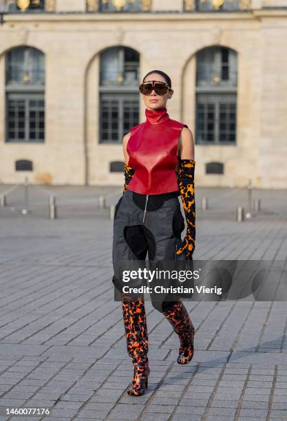 Sabina Jakubowicz wears red sleeveless turtleneck, grey black high waisted pants with zipper, gloves with flame print, boots with animal print,...