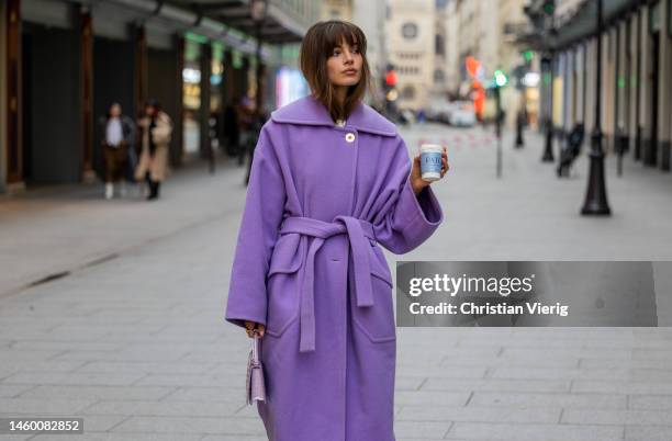 Mara Lafontan with to go coffee with logo print wears lavender belted wool coat, black pants, pink bag outside Patou at La Samaritaine on January 27,...