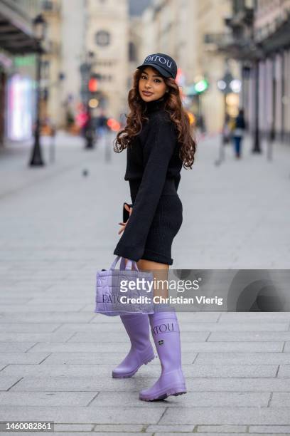 Guest wears black cap with logo print, black turtleneck with long sleeves, knitted shirts, purple bag, knee high socks, rain boots outside Patou at...