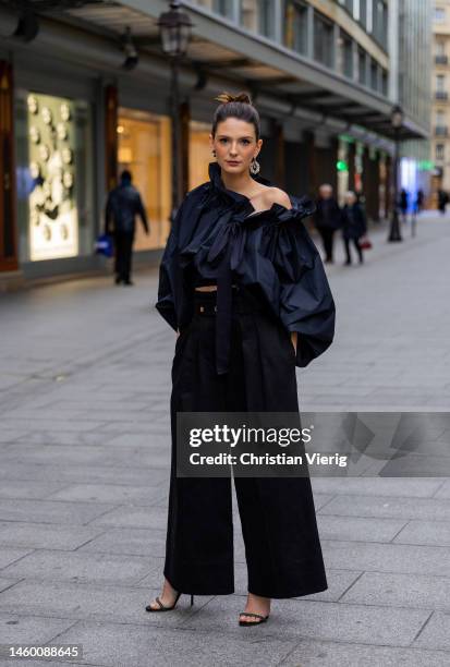 French actress Josephine Japy wears black asymmetric ruffled blouse with puffy long sleeves, black high waist pants, pearl earring, heels sandals...